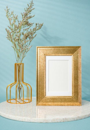 blank luxury gold photo frame with flower vase decor on stone table wtih blue backgroundの写真素材