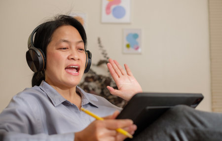 asian woman waving hand greeting when video conference online at home with relax poseの写真素材