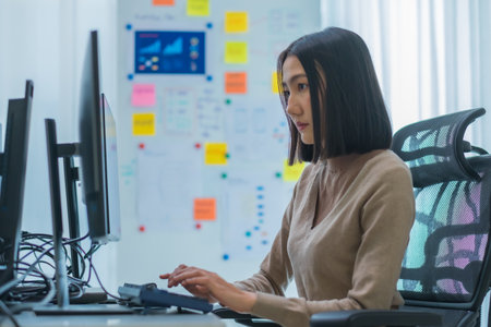 Asian promt engineer develope coding app with software data sitting in front of computer monitor at...