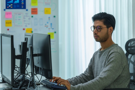 Asian man  prompt engineer develop coding app with software data sitting in front of computer monitor at officeの写真素材