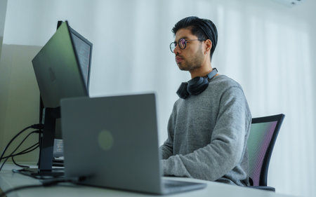 Asian man  prompt engineer develop coding app with software data sitting in front of computer monitor at officeの写真素材