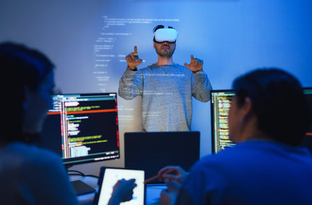 developer uses a VR headset to interact with projected interface designs, while colleagues discuss and code on screens, highlighting the integration of virtual reality and UI/UX design in modern software development.の写真素材