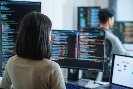 Asian software developers working on multiple screens displaying code and application diagrams in a modern officeの写真素材