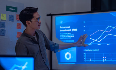 asian leader present  business presentation in a dimly lit office, analyzing financial charts and data projections on a screenの写真素材