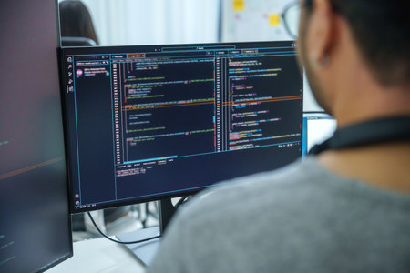 Asian software developers working on multiple screens displaying code and application diagrams in a...
