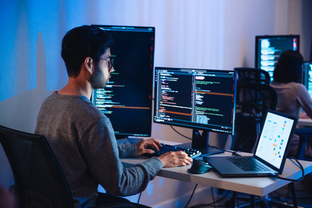 Asian software developers working on multiple screens displaying code and application diagrams at night in modern officeの写真素材