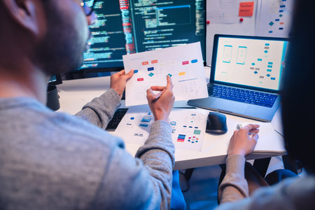 Asian software developers teams working on multiple screens displaying code and application diagrams at night in modern officeの写真素材