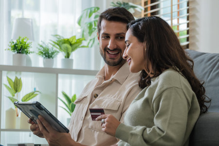 hispanic Couple using tablet and credit card to shop online through e-commerce app, making payment and browsing modern platform with promo codes and discount offersの写真素材