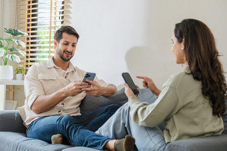 Hispanic Couple sitting together but emotionally distant, ignoring each other while using smartphones and social media at homeの写真素材