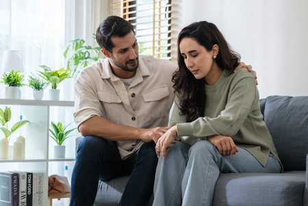 Supportive couple in emotional moment at home as woman struggles with sadness and stress, expressingの写真素材