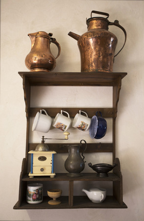 Old dishes. Historical Cookware. Old hunged on wooden shelf on medieval wall. Antique equipment hanged design, cup, mug, kettle, coffee grinder, small mill, salt cellar and saucepan.のeditorial素材