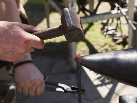 Blacksmith forge with hammer iron on anvil. Detail of working hands. Daily sunshineの写真素材