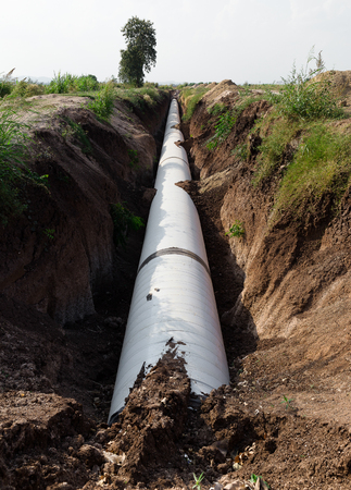 Close up large concrete pipe under loamy sand mounds to the rural dirt road.の写真素材
