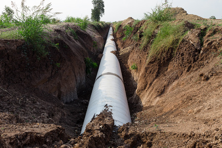 Close up large concrete pipe under loamy sand mounds to the rural dirt road.の写真素材