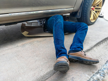 Mechanic in blue uniform lying down and working under car at auto service garageの写真素材