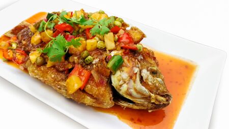 Deep Fried Fish with Chili Sauce (Pla Rad Prik) and herb topped on ; tomato Bell pepper garlic Tamarind Parsley . on brown dish in white background. Thai traditional food styleの写真素材