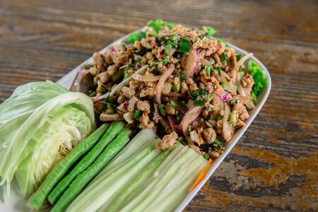 Spicy minced pork salad or Ground pork salad (Laab) is a Thai food for health consists of pork ground rice chili lemon onion and herb mixed in plate on a wood table at Thai street foodの写真素材