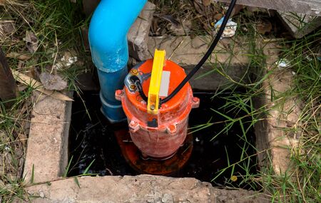 Heavily used old partially submerged metal water pump pumping water from flooded backyard through...