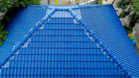A roof of a house or cottage made of blue metal tiles with drains, slopes and chimney against the blue skyの写真素材