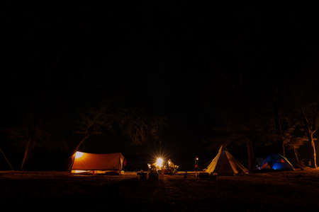 Traveling and camping concept - camp tent at night under a sky full of stars. Orange illuminated...