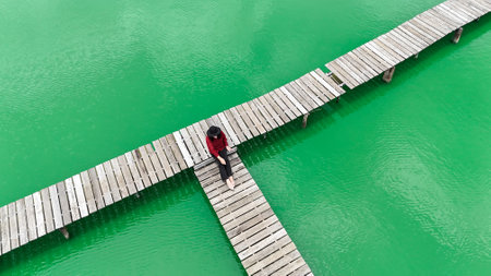 The young woman sitting on a wooden jetty dangling her legs above the water and looking down