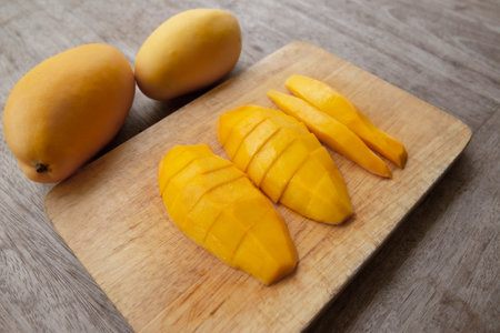 whole mango fruits on wooden table and cut into slices. Large juicy bright ripe yellow fruitsの写真素材
