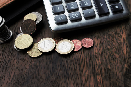 Money (coins) euros, calculator and some stationery on wood table, top view financial background concept. vintage tone.の写真素材