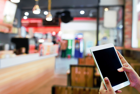 Hand hold and touch screen tablet,with abstract blur coffee shop.の写真素材