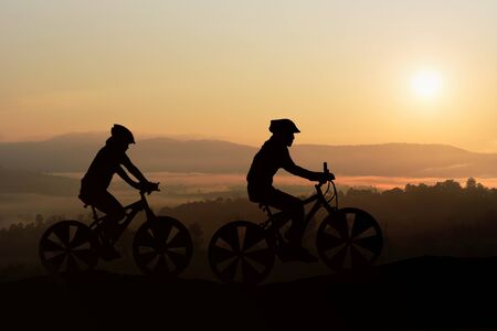 Silhouettes Man and Girl are bicycle on mountain in the sunlight