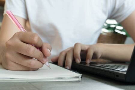 Young business woman sitting at table with laptop and taking notes in notebook.