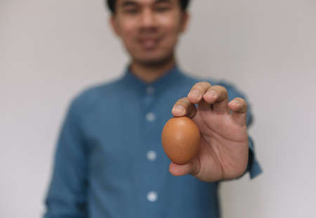 Male hand holding Easter brown chicken egg isolated on grey backgroundの写真素材