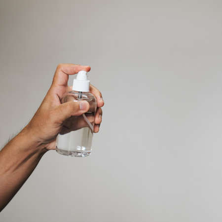 Handsome man holding alcohol spray bottle for hygiene cleaner on grey background.の写真素材