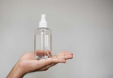 Handsome man holding alcohol spray bottle for hygiene cleaner on grey background.の写真素材