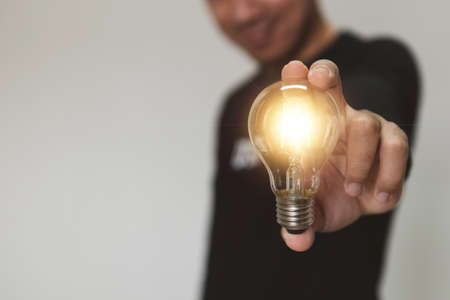 Hand holding a light bulb rises up with investment for business growth and dollar yuan yen euro and pound sterling sign. Global currency exchange conceptの写真素材