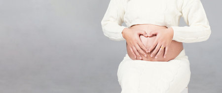 Pregnant woman in white dress holds hands on belly on a white background. Pregnancy, maternity,...