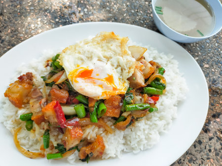 Fried rice with crispy pork basil, a fried egg with sliced ââlong beans and fresh red peppers in a white plate placed on a stone table at a restaurant.の写真素材
