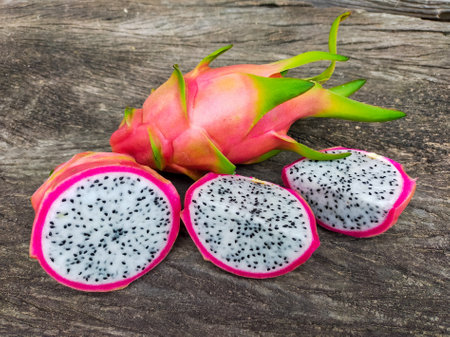 Juicy pink dragon fruit with white flesh and black seeds lying on old wooden background.の写真素材