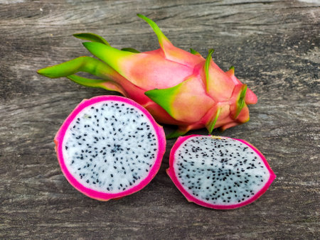 Juicy pink dragon fruit with white flesh and black seeds lying on old wooden background.の写真素材