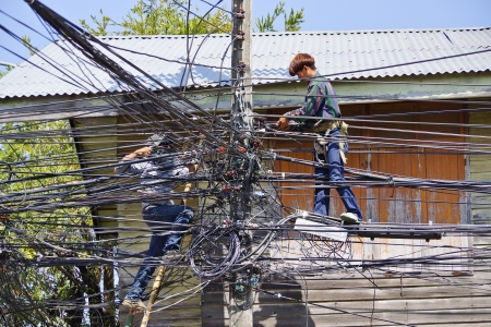 Ubon Ratchathani, Thailand - January 20, 2014  Two Thai electricians are fixing confusing electricity lines on a pole のeditorial素材