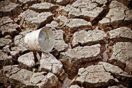 empty watering bucket on dried, cracked earth without water leftの写真素材