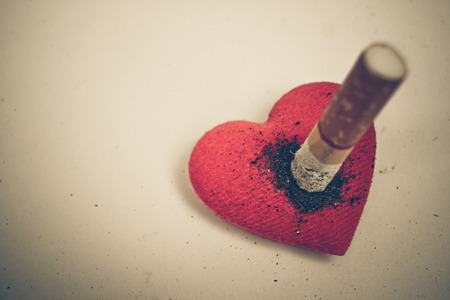 Cigarette burnt a red heart - smoking destroying health conceptの写真素材