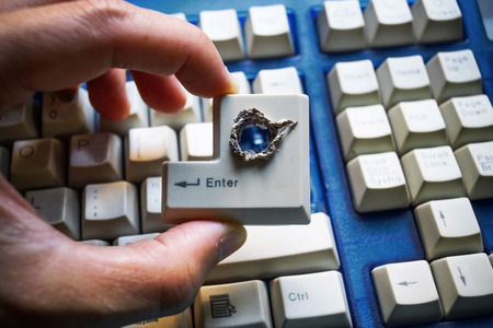 Hacker's hand picking up computer enter button with a hole representing computer security breachの写真素材