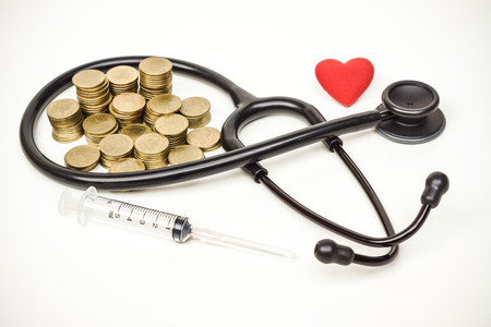 a stethoscope with piles of coins, a syringe, and a red heart - healthcare cost conceptの写真素材