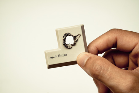 hacker's hand holding computer enter button with a hole  computer security breach conceptの写真素材