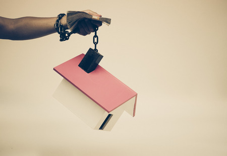 hand holding a pile of banknote and chained with a houseの写真素材