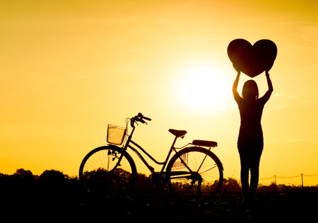 Silhouette of a woman with a bicycle and holding big heartsの写真素材