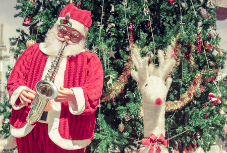 Santa Clause playing trumpet with a white reindeer and a big Christmas treeの写真素材