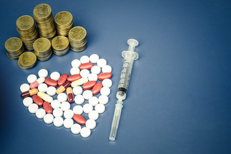A syringe on medicine arranged as a heart shape with stacks of golden coinsの写真素材