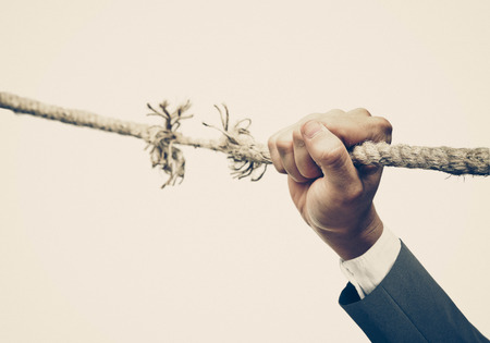 Hand of a businessman hung on almost torn apart rope - Business risk conceptの写真素材