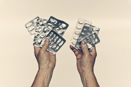 Patient's hand holding a collection of used tablets covers in vintage tone - Drug overuse - drug abuse conceptの写真素材
